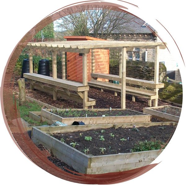 An outdoor learning zone with seating under an arbor, raised beds and a secure storage shed